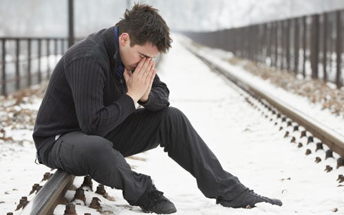 Man with seasonal affective disorder sitting on railroad track